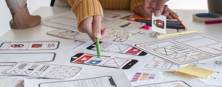 Image of a team of developers brainstorming UI and UX design ideas for a mobile app on a paper wireframe interface. Planning the user interface development team for an intuitive UI design.