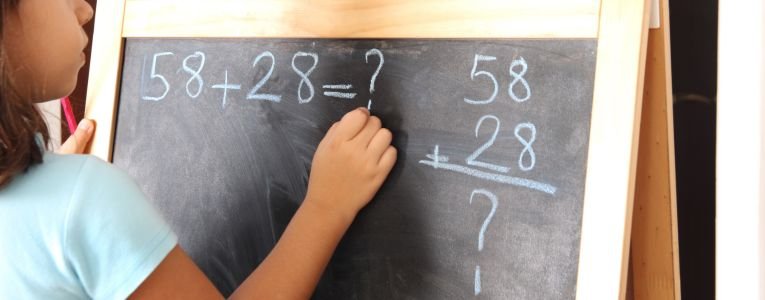 Little girl writing mathematics operations on blackboard