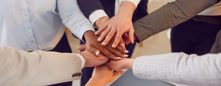 Team of colleagues shows unity and willingness to work together by folding their hands together.